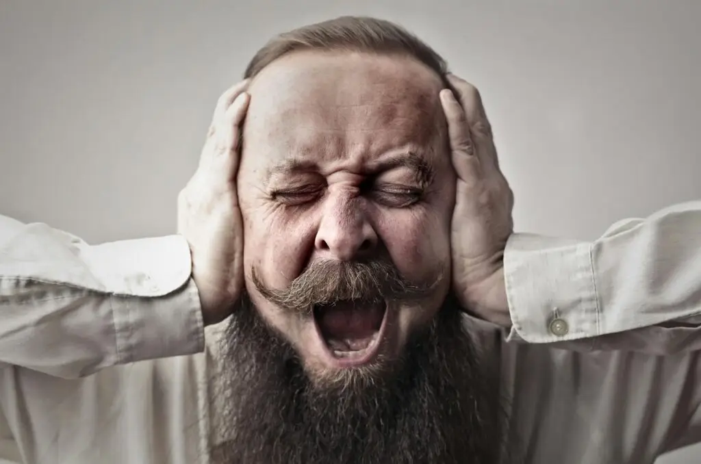 7 kluczowych różnic między hiperakuzją a mizofonią — szybki przewodnik kliniczno-praktyczny + plan na 30 dni Portrait of a man with facial hair, covering his ears and screaming, expressing stress or frustration.